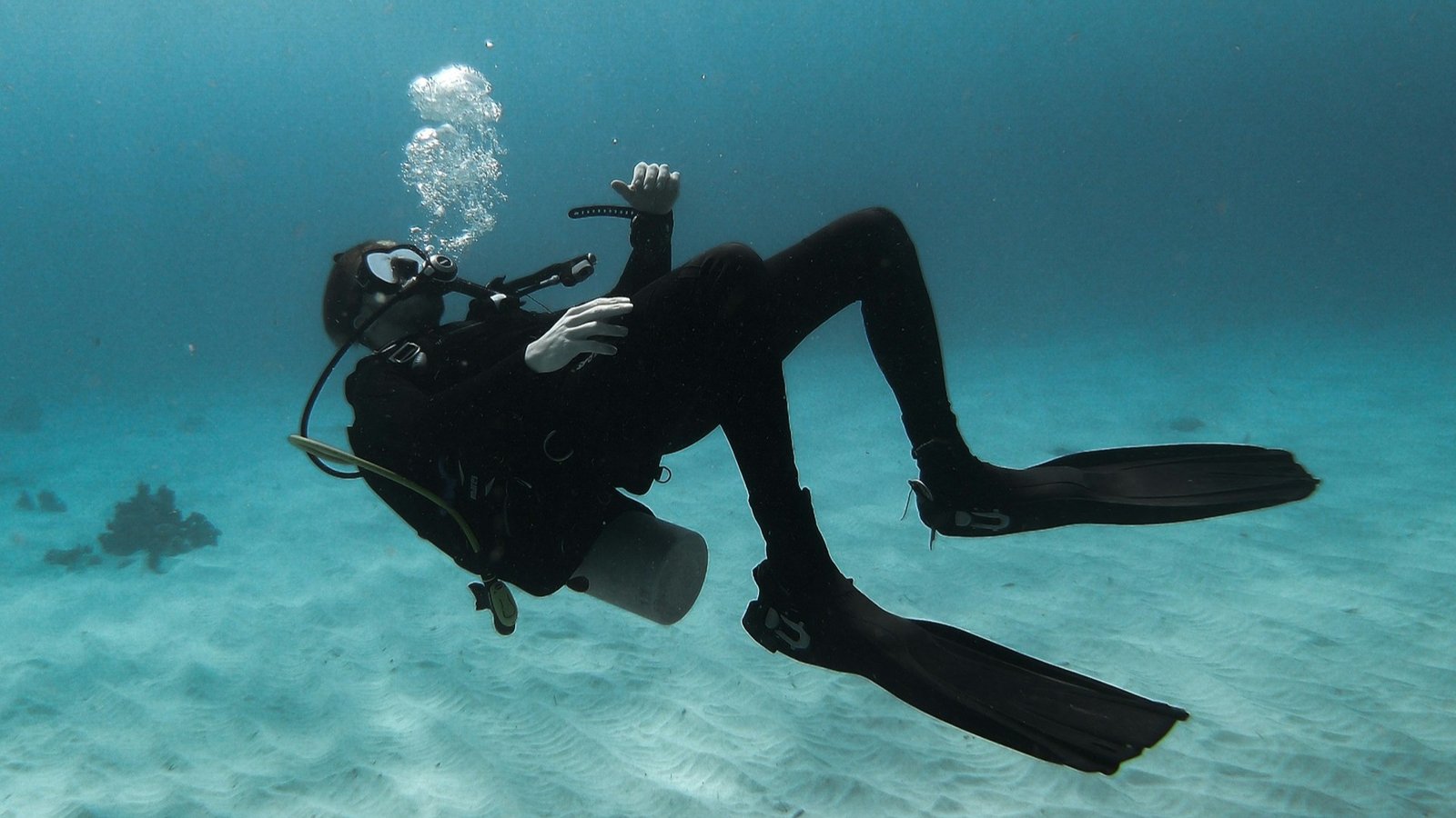 Scuba diver exploring the ocean while swimming near sandy seabed